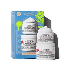 A graphic featuring a blue Kiehl’s gift box on the left. The box contains two white jars of "KIEHL’S ULTRA FACIAL CREAM." To the right of the box, two more jars are displayed, with the top one open to reveal a swirl of white cream. The box has bright green graphic paint splatters and a bow design, and features the text "HYDRATION 2 THE MAX" on the front.